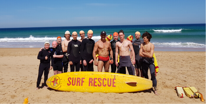 Students and staff on the beach with a surf rescue board at Surf Camp