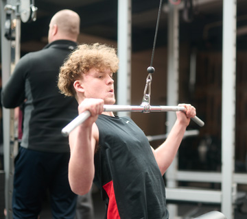 A coach supervising a student on a cable machine